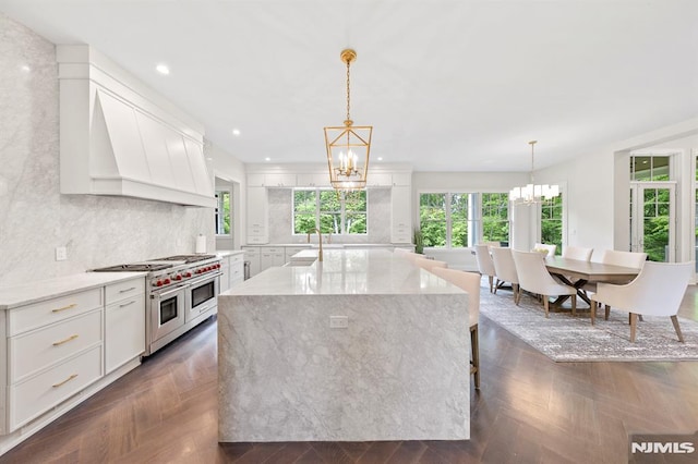 kitchen featuring light stone counters, white cabinets, decorative light fixtures, and range with two ovens