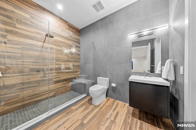 bathroom with vanity, a shower with door, toilet, tile walls, and wood-type flooring