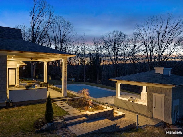 pool at dusk featuring ceiling fan and a patio