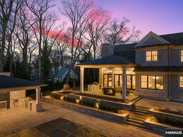 back house at dusk featuring a patio area and exterior kitchen