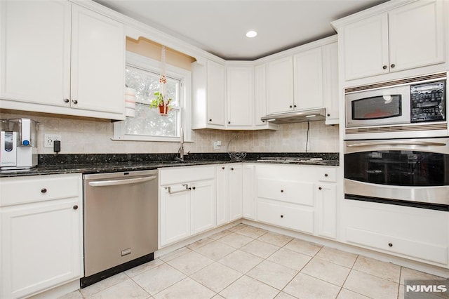 kitchen with dark stone countertops, white cabinetry, appliances with stainless steel finishes, light tile patterned flooring, and sink