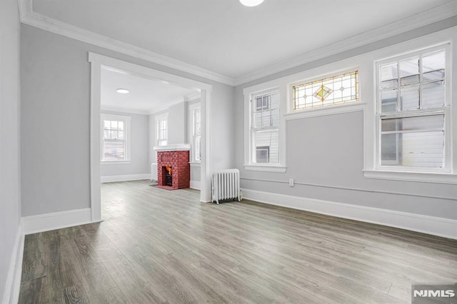 unfurnished living room featuring hardwood / wood-style flooring, a brick fireplace, radiator, and crown molding