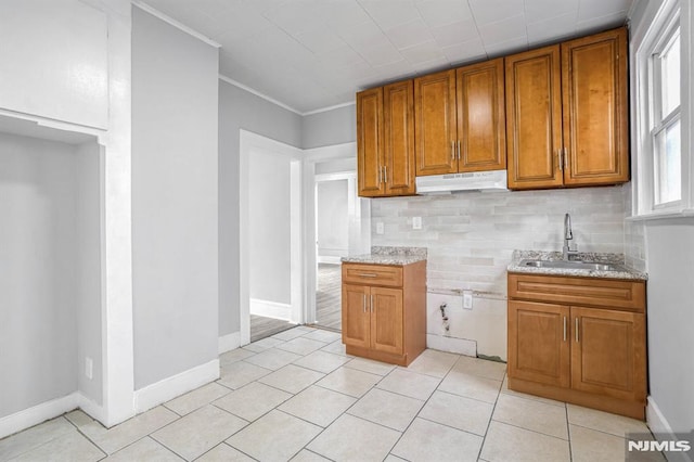 kitchen featuring light stone countertops, sink, backsplash, light tile patterned floors, and ornamental molding