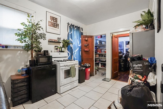 kitchen featuring light tile patterned floors, white gas range oven, and fridge