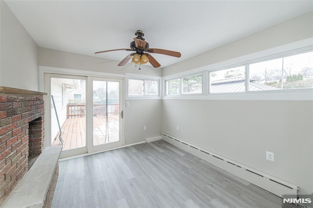 interior space with a fireplace, a baseboard radiator, light hardwood / wood-style floors, and a healthy amount of sunlight