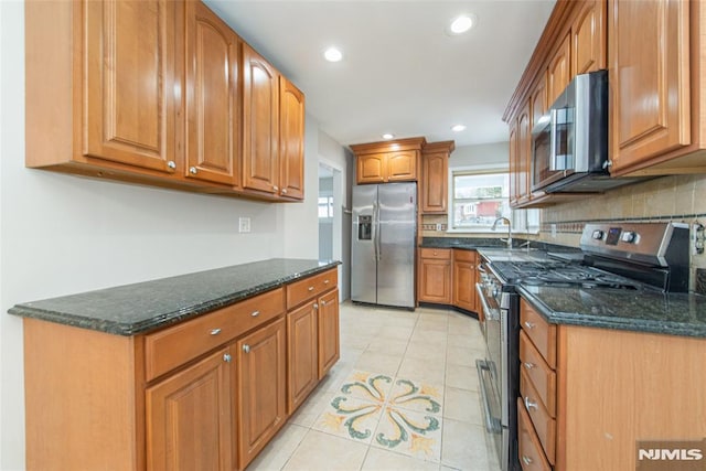 kitchen with appliances with stainless steel finishes, dark stone countertops, light tile patterned flooring, and sink