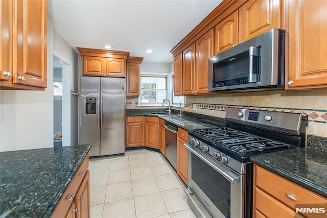 kitchen featuring sink, light tile patterned floors, dark stone counters, and appliances with stainless steel finishes