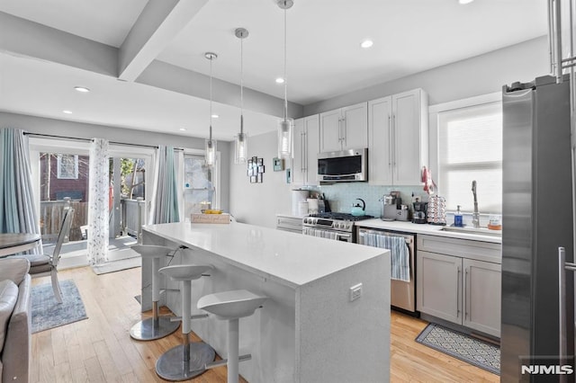 kitchen with decorative backsplash, appliances with stainless steel finishes, a breakfast bar, sink, and decorative light fixtures