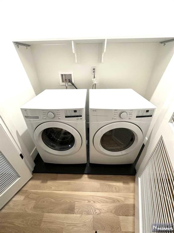 clothes washing area with washing machine and clothes dryer and light hardwood / wood-style flooring