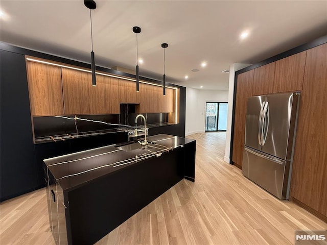 kitchen with a center island, sink, hanging light fixtures, light hardwood / wood-style flooring, and stainless steel fridge