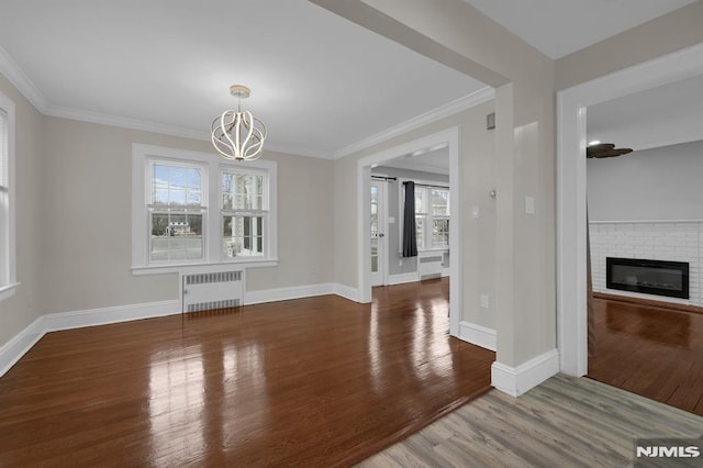 unfurnished dining area with wood-type flooring, radiator heating unit, ornamental molding, and a brick fireplace