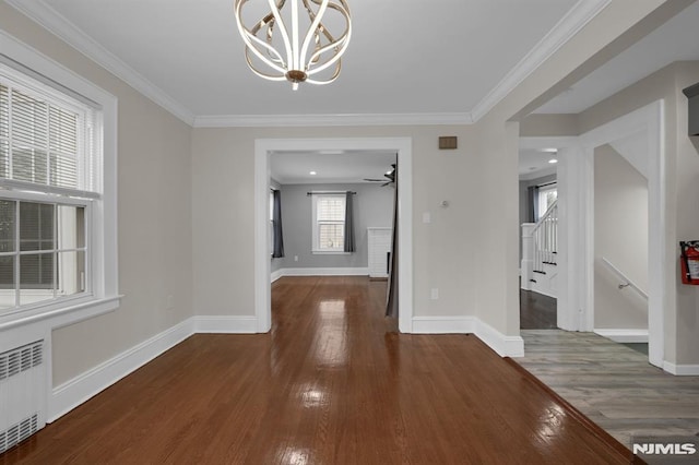 unfurnished dining area featuring ceiling fan with notable chandelier, radiator heating unit, dark hardwood / wood-style flooring, and crown molding