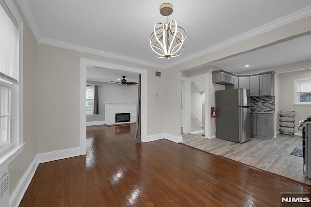 interior space with ceiling fan with notable chandelier, crown molding, light wood-type flooring, and a fireplace