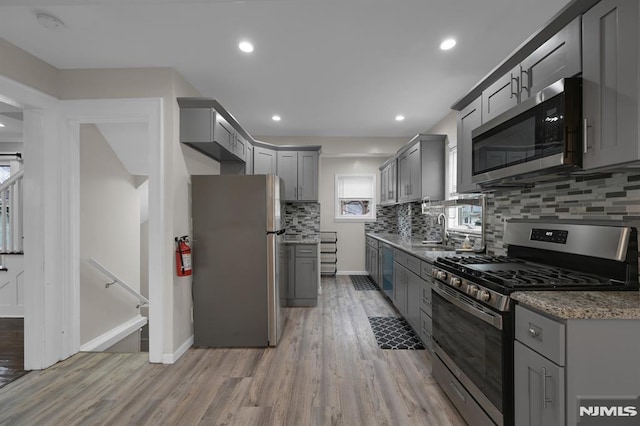 kitchen with backsplash, sink, light hardwood / wood-style flooring, gray cabinets, and stainless steel appliances