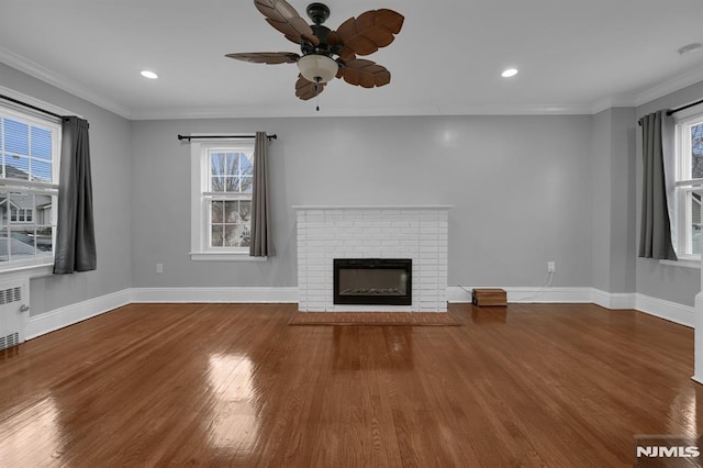 unfurnished living room featuring radiator, ceiling fan, crown molding, wood-type flooring, and a fireplace