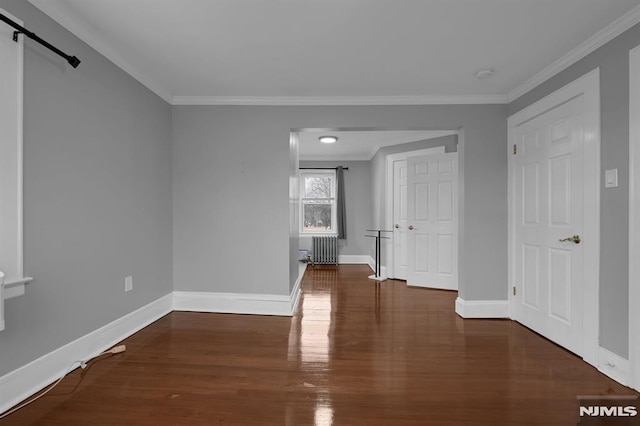 empty room featuring a barn door, radiator heating unit, crown molding, and dark wood-type flooring