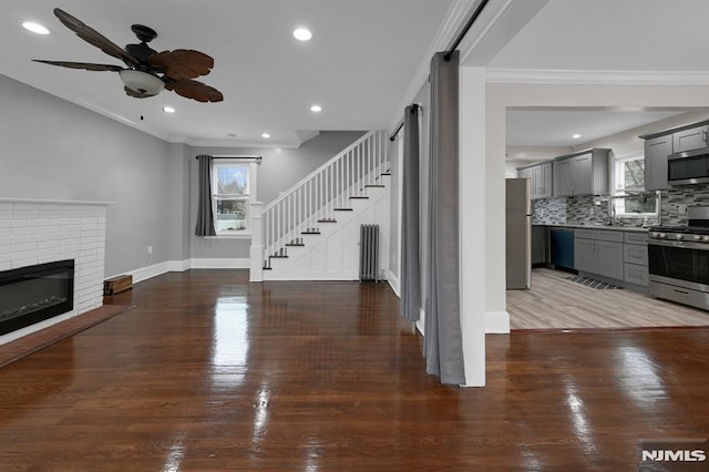 unfurnished living room featuring ceiling fan, sink, dark hardwood / wood-style floors, a fireplace, and ornamental molding