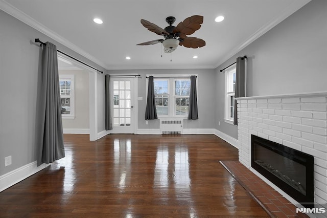 unfurnished living room with a brick fireplace, ornamental molding, ceiling fan, dark wood-type flooring, and radiator heating unit