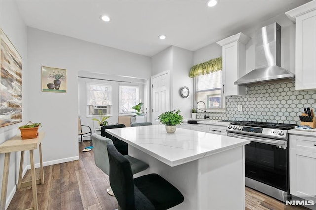 kitchen with gas range, white cabinetry, a kitchen island, and wall chimney range hood