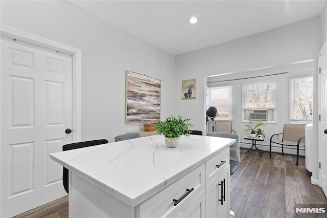 kitchen with light stone countertops, dark hardwood / wood-style flooring, baseboard heating, white cabinets, and a center island