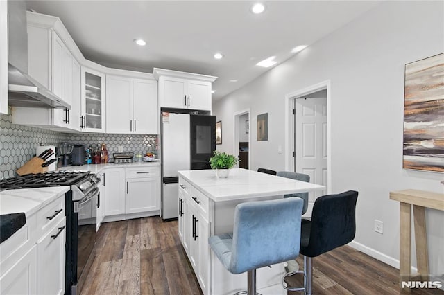 kitchen featuring a breakfast bar, range with gas cooktop, white cabinetry, and wall chimney range hood