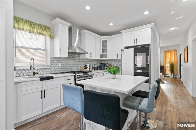 kitchen with white cabinets, light stone counters, wall chimney exhaust hood, and stainless steel range with gas stovetop