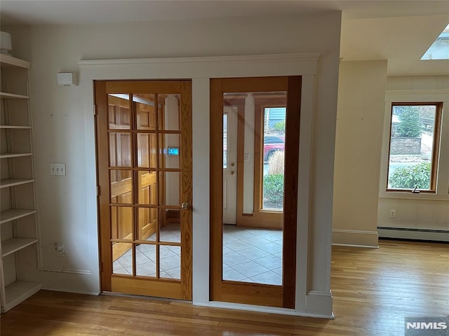 doorway with light hardwood / wood-style floors, baseboard heating, french doors, and a wealth of natural light