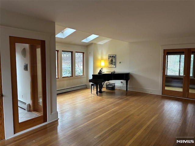 miscellaneous room featuring light hardwood / wood-style flooring, vaulted ceiling with skylight, and a baseboard heating unit