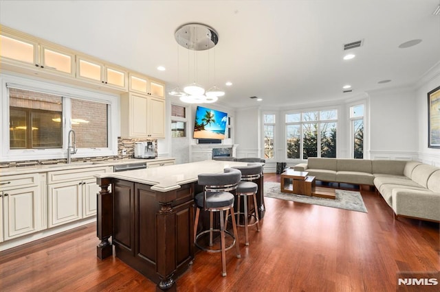 kitchen with a breakfast bar area, crown molding, pendant lighting, a kitchen island, and sink