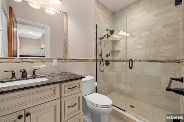 bathroom featuring toilet, vanity, tile walls, decorative backsplash, and a shower with shower door