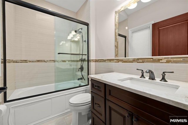 full bathroom with toilet, tasteful backsplash, tile walls, shower / bath combination with glass door, and vanity