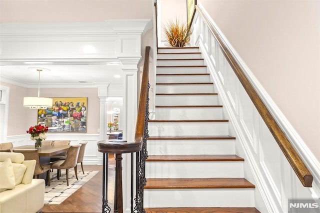 staircase with ornamental molding, hardwood / wood-style flooring, and decorative columns