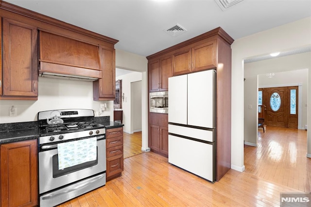 kitchen with appliances with stainless steel finishes, light wood-type flooring, and dark stone counters