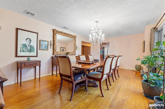 dining space with an inviting chandelier, light wood-type flooring, and a textured ceiling