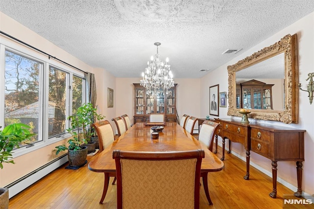 dining room featuring a textured ceiling, a baseboard heating unit, light hardwood / wood-style floors, and a notable chandelier