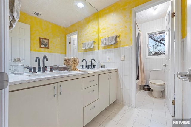 full bathroom featuring a textured ceiling, tile walls, vanity, and toilet