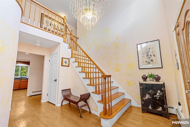 stairway with a baseboard radiator, a notable chandelier, a towering ceiling, and wood-type flooring