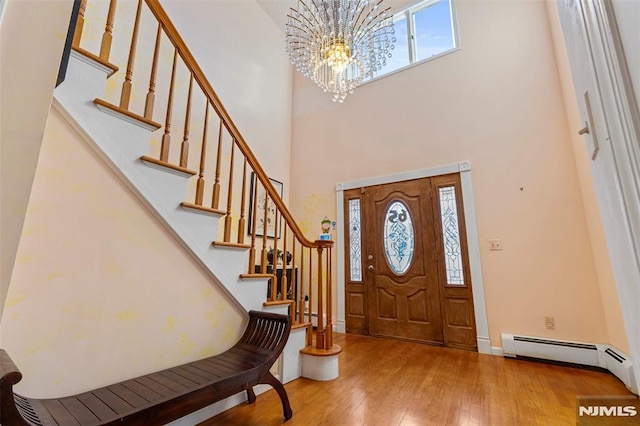 entrance foyer featuring a towering ceiling, baseboard heating, a chandelier, and light hardwood / wood-style flooring