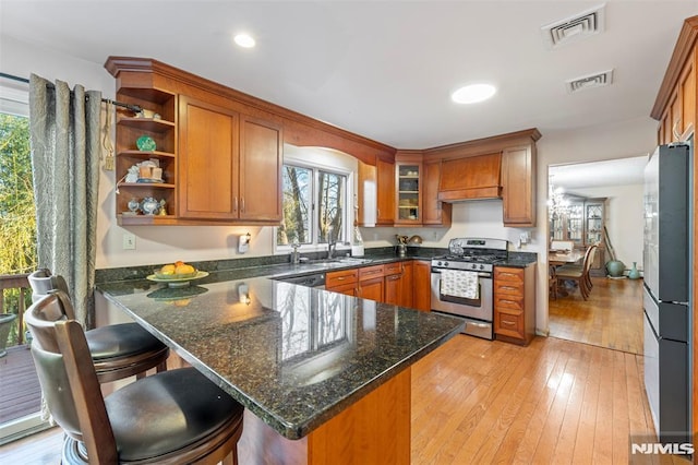 kitchen with fridge, stainless steel range with gas cooktop, dark stone counters, and kitchen peninsula