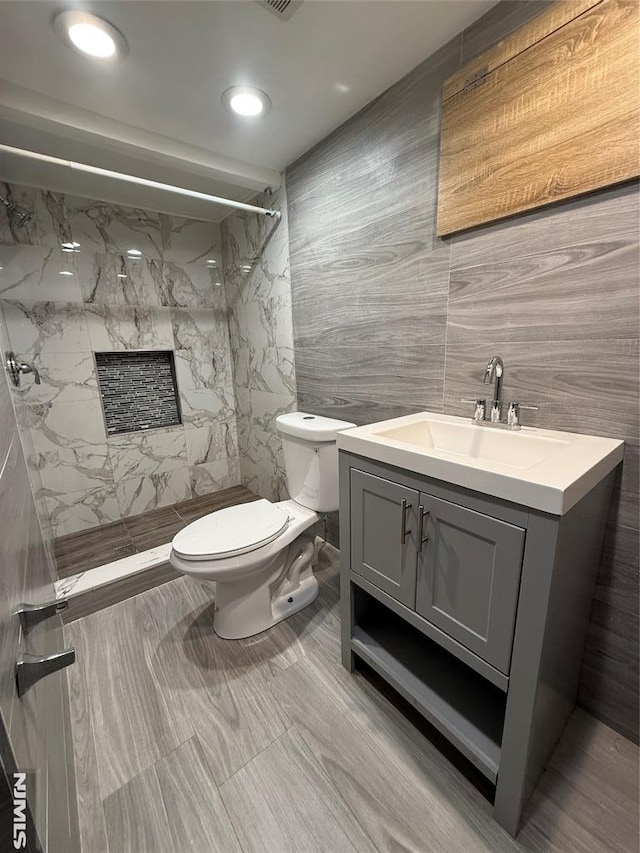 bathroom with a tile shower, vanity, toilet, and tile walls