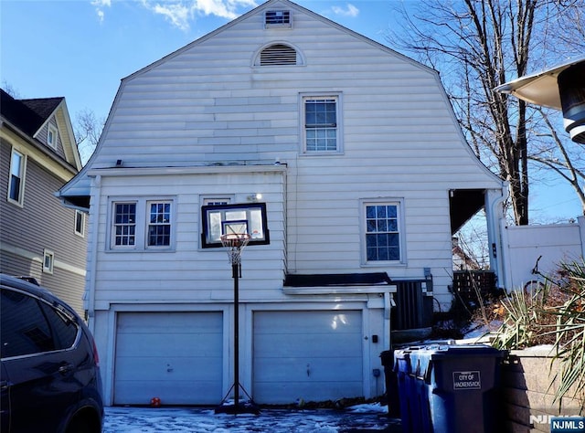 snow covered back of property featuring central AC unit and a garage