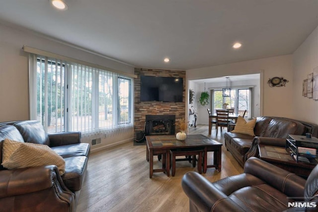 living room with a stone fireplace, light hardwood / wood-style floors, and plenty of natural light