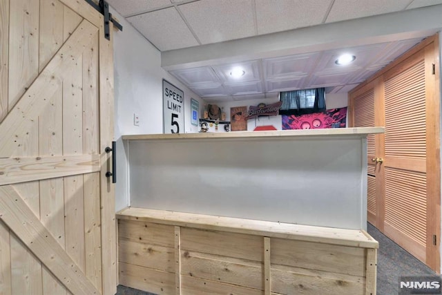 interior space featuring light brown cabinets, a drop ceiling, and a barn door