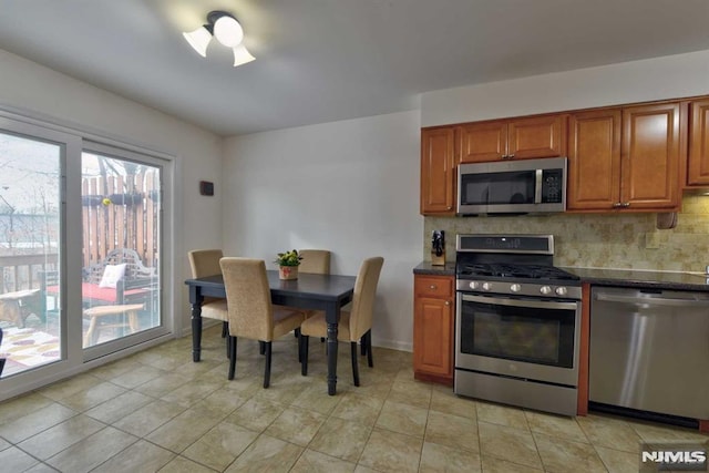 kitchen featuring dark stone counters, stainless steel appliances, tasteful backsplash, and light tile patterned floors