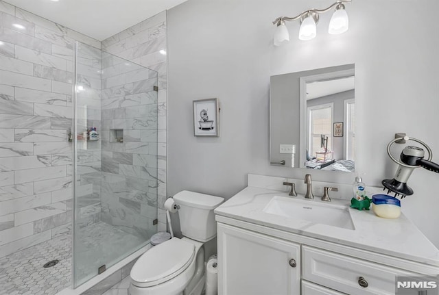 bathroom with a tile shower, vanity, and toilet