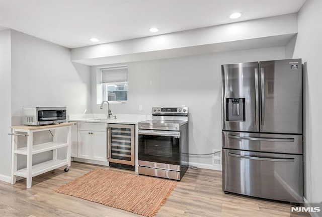 kitchen with appliances with stainless steel finishes, beverage cooler, sink, light hardwood / wood-style flooring, and white cabinets