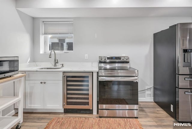 kitchen featuring light stone countertops, sink, stainless steel appliances, wine cooler, and white cabinets