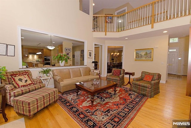 living room featuring a towering ceiling, an inviting chandelier, and light wood-type flooring