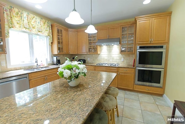 kitchen featuring sink, light stone counters, a kitchen bar, hanging light fixtures, and appliances with stainless steel finishes