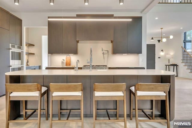 kitchen with a large island with sink, gray cabinets, light hardwood / wood-style flooring, and a breakfast bar area